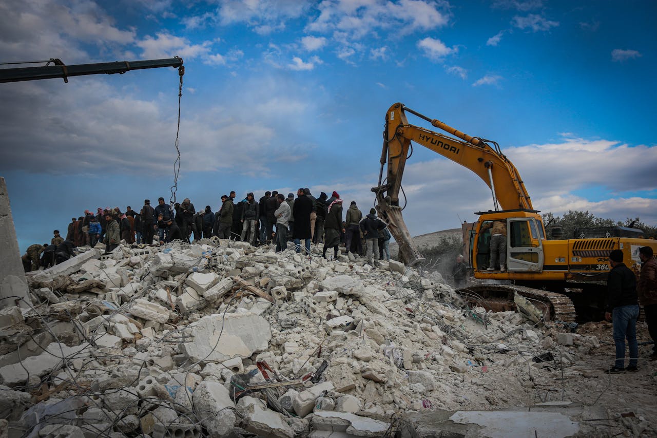 Home Rescue workers and excavator at disaster site in Idlib, Syria, removing debris.